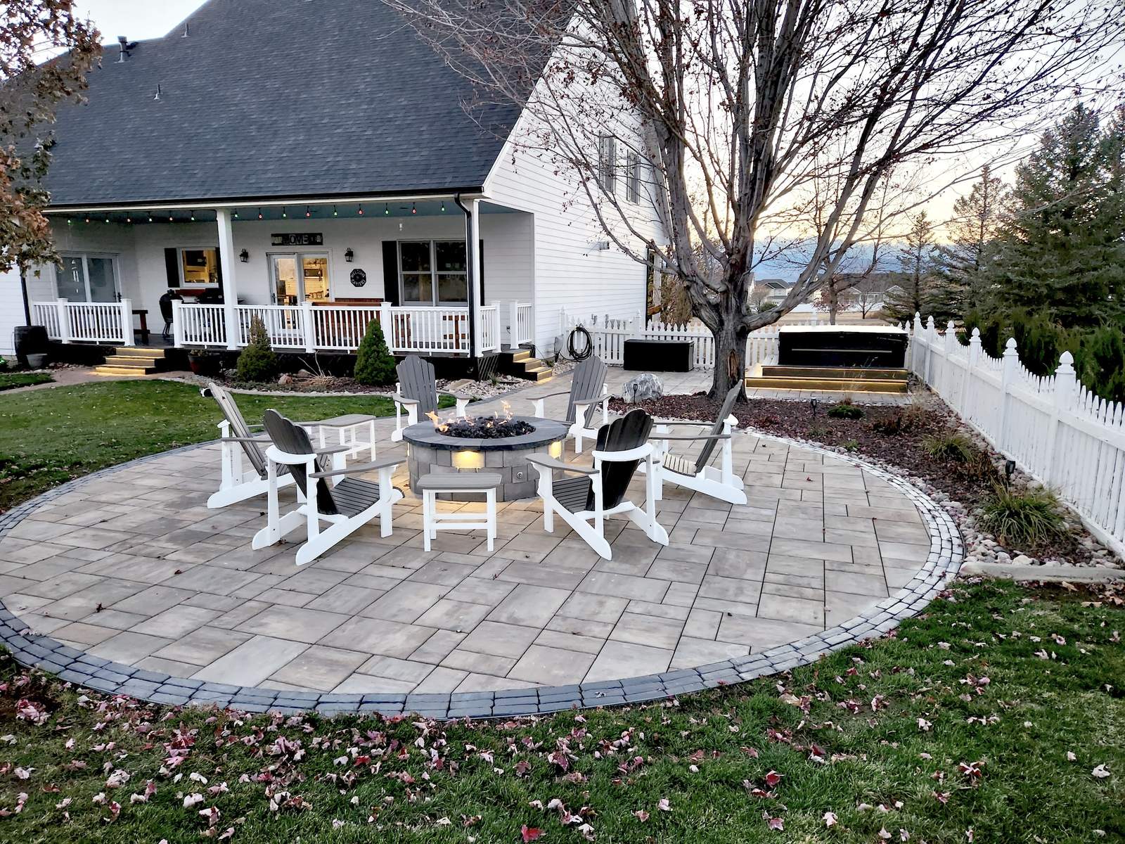 Farmhouse-style paver patio with a gas fire pit ringed by Adirondack chairs