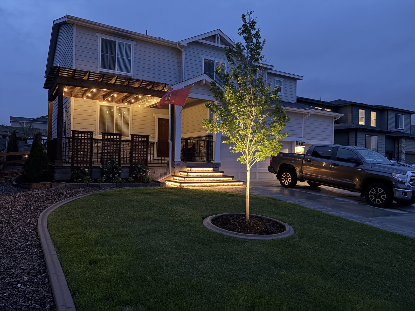 Front yard landscape lighting with an uplit tree, lit trellis, and warm step lighting