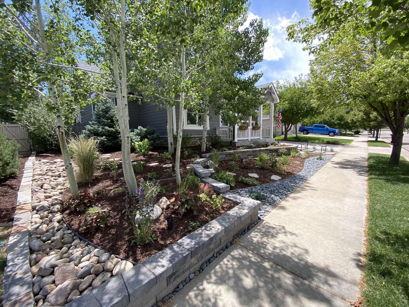 Front yard planting beds with perennials, aspens, and a block retaining wall along the walk