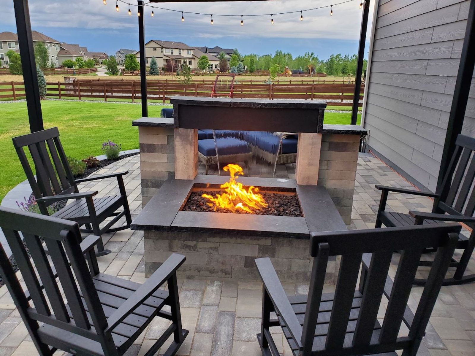 Outdoor fireplace combining an open gas fire and a falling water sheet, ringed by rocking chairs