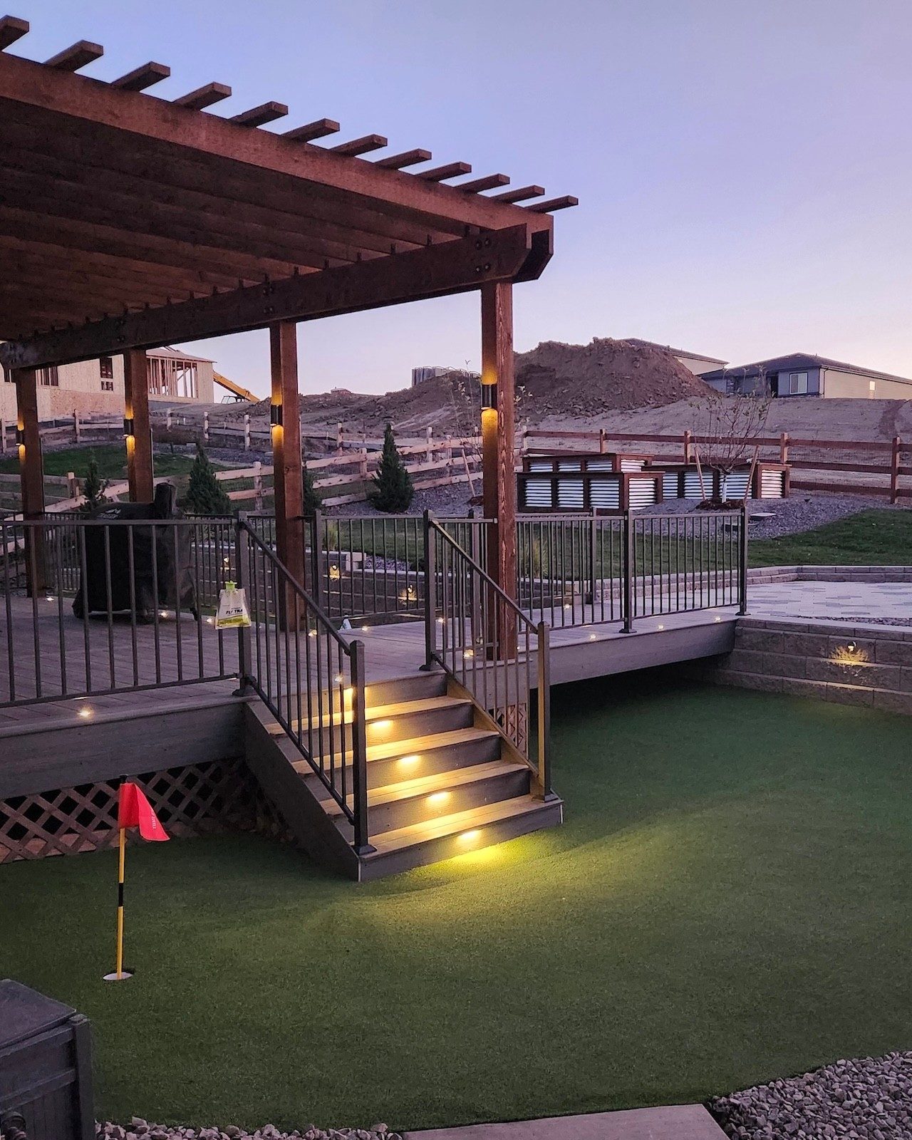 Cedar pergola deck with lit stairs down to a backyard putting green at dusk